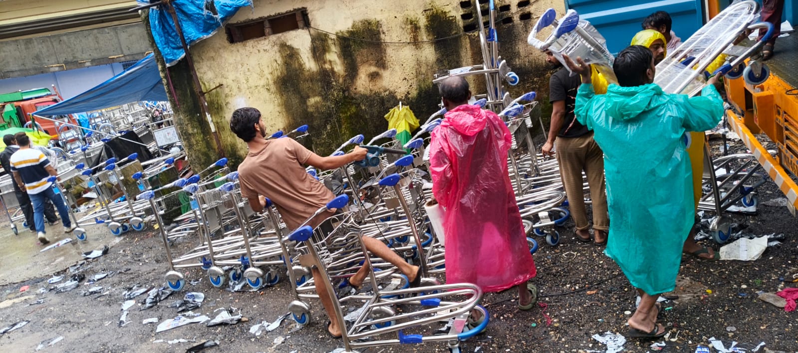 Staff carrying shrink-wrapped airport luggage trolleys during delivery in rain